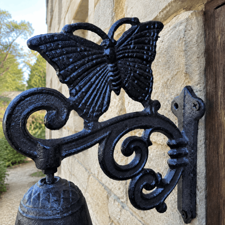 Close-up view of a cast-iron butterfly doorbell for a garden gate