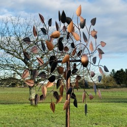 Amboise, decorative garden wind spinner in copper-toned metal, side view in a garden setting