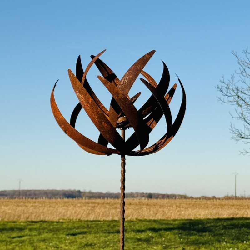Decorative garden wind spinner in rustic metal, 220 cm tall, installed in a garden