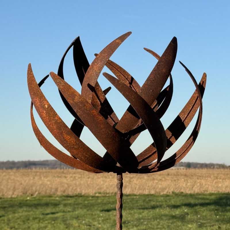 Full view of the sculptural decorative garden wind spinner in rusted metal under a clear sky
