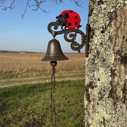 Cast iron wall bell with ladybug, set in a charming rustic garden scene